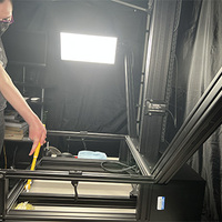 An image of the 413 copy stand from the side. The tabletop has been removed, showing the empty space below the top, one of the lights, and the center column. A woman in black wearing a dust mask is cleaning the copy stand with a swiffer duster.