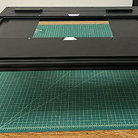 A square table made of black aluminum and wood. It has four legs, and there is an empty space in the center of the table. There are two rubberized knobs on the end nearest the camera, and two low grips on the side away from the camera.